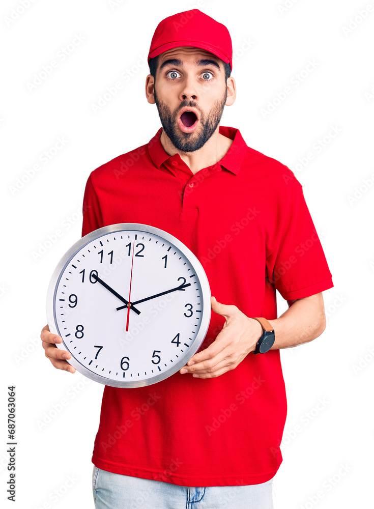 Young handsome man with beard wearing delivery uniform holding big clock scared and amazed with open mouth for surprise, disbelief face Young handsome man with beard wearing delivery uniform holding big clock scared and amazed with open mouth for surprise, disbelief face
