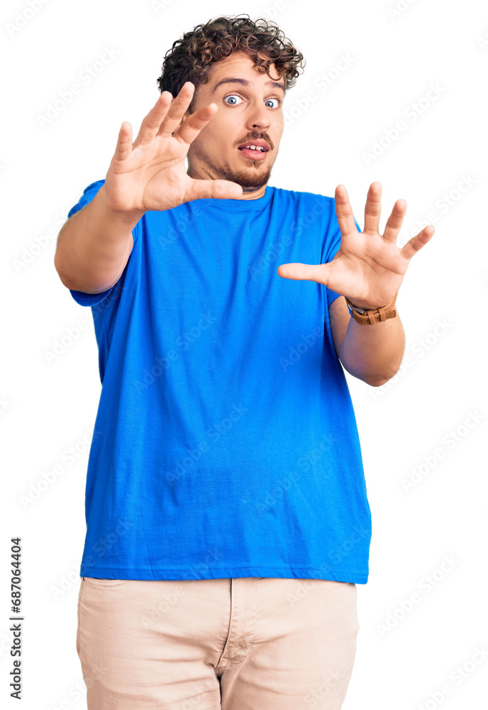Naklejka premium Young handsome man with curly hair wearing casual clothes afraid and terrified with fear expression stop gesture with hands, shouting in shock. panic concept.