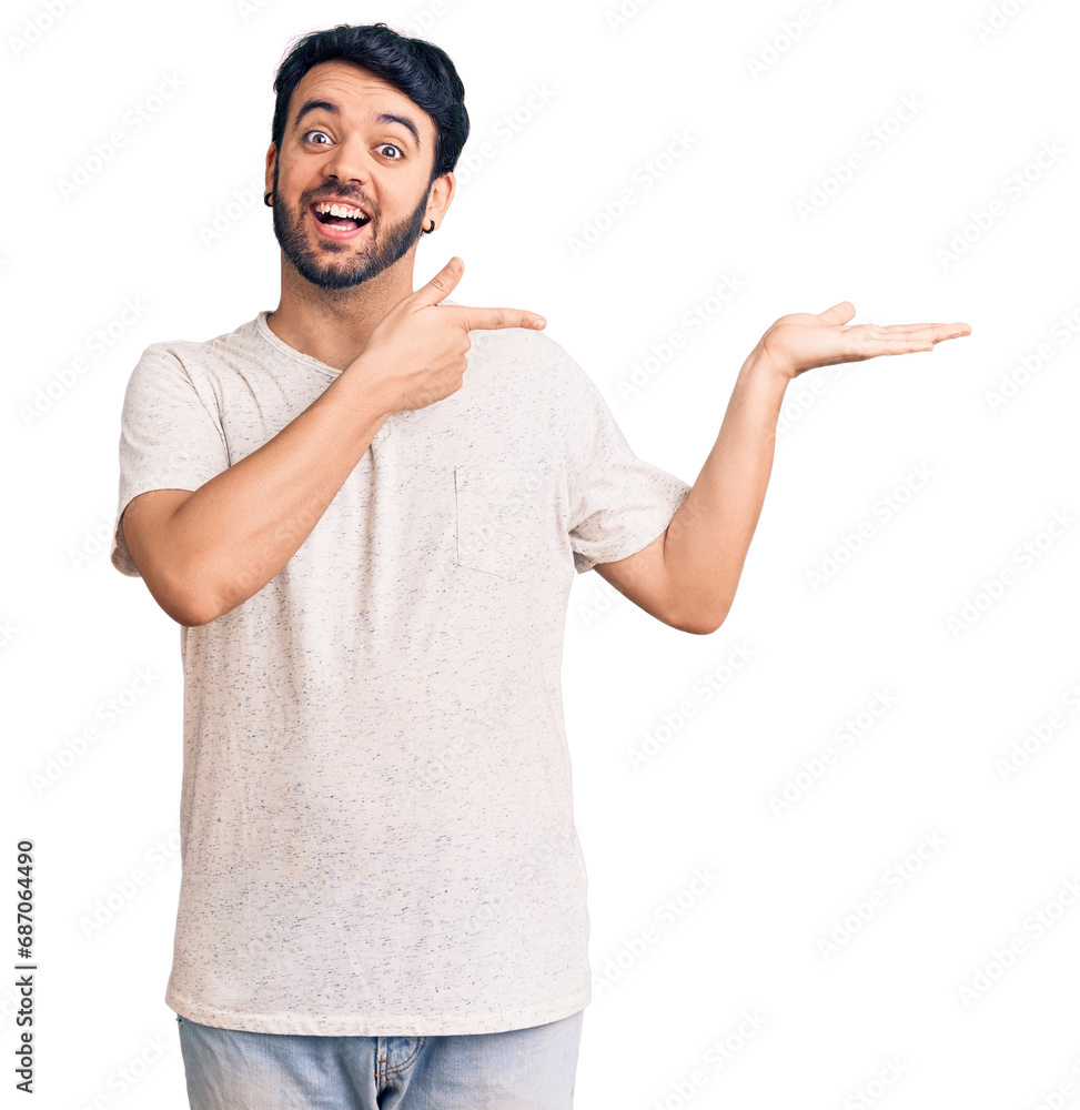 Young hispanic man wearing casual clothes amazed and smiling to the camera while presenting with hand and pointing with finger. Young hispanic man wearing casual clothes amazed and smiling to the camera while presenting with hand and pointing with finger.