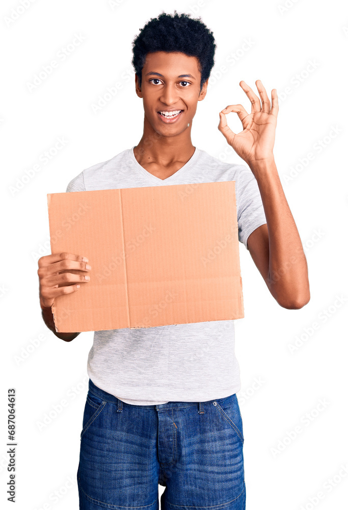 Young african american man holding banner cardboard doing ok sign with fingers, smiling friendly gesturing excellent symbol Young african american man holding banner cardboard doing ok sign with fingers, smiling friendly gesturing excellent symbol