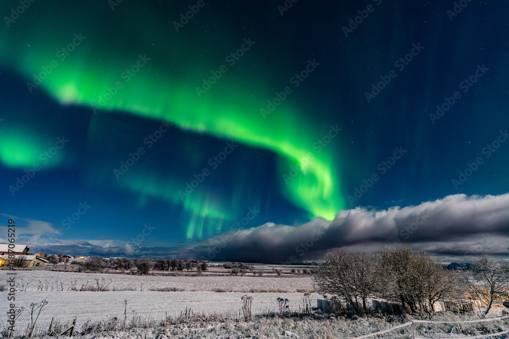 aurora borealis over norwegian fileds covered with snow and over a stormy cloud