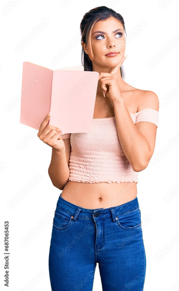 Young beautiful woman holding book serious face thinking about question with hand on chin, thoughtful about confusing idea Young beautiful woman holding book serious face thinking about question with hand on chin, thoughtful about confusing idea