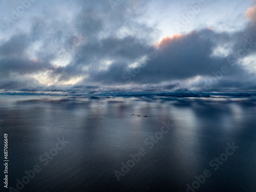aerial view over fjord with clouds reflecting in water and mountains with snow on background in norway