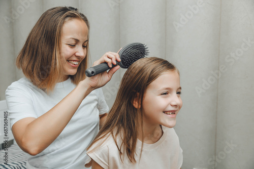 a little dark-haired girl looks into the camera and smiles while her mother combs her daughter's hair. hair care