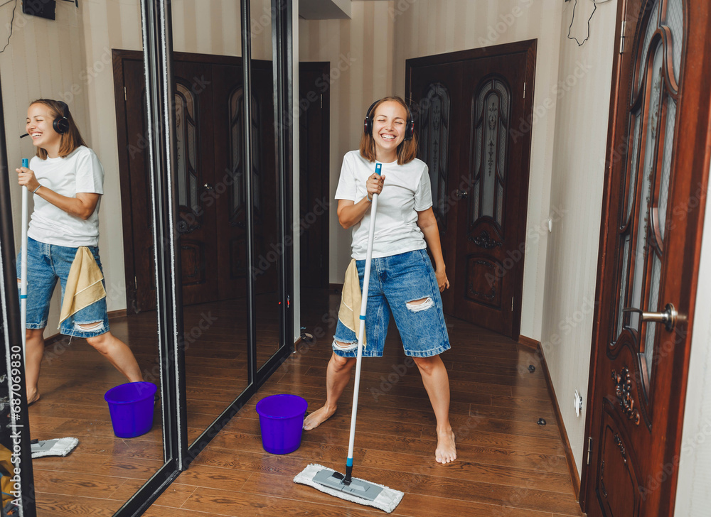 Happy young woman cleaning her house, singing with a mop like a microphone and having fun. housewife enjoying household chores, creatively cleaning the house