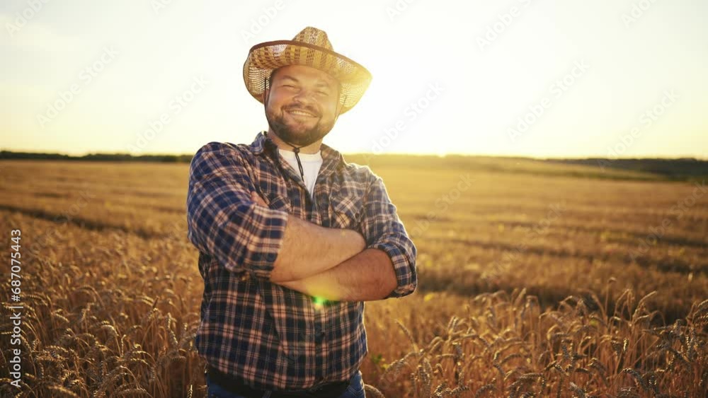 Happy bearded farmer in hat looking at camera standing on agricultural wheat field with combine harvester and dump truck on background. Harvesting, farming at sunset. Food production, agribusiness. Happy bearded farmer in hat looking at camera standing on agricultural wheat field with combine harvester and dump truck on background. Harvesting, farming at sunset. Food production, agribusiness.