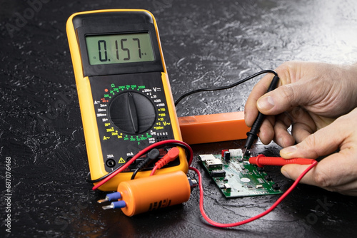 An electrician takes readings from a microcircuit using a multimeter. Measuring instruments. Copy space. Voltage measuring tool. Checking battery voltage. Male hands repairing a microcircuit.