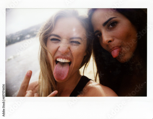 Two Friends Sticking Out Tongues At Camera. Instant close-up of two beautiful young girls making sign of horns and sticking out tongues.Backlit. photo