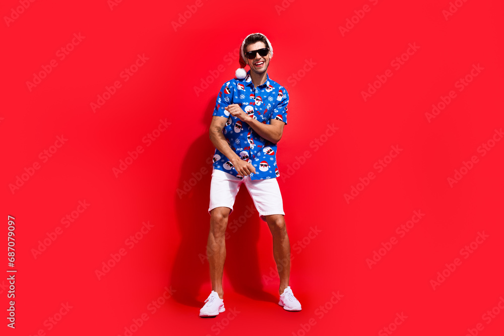 Full body photo of handsome young guy energetic dancer dressed santa claus print x-mas outfit isolated on red color background