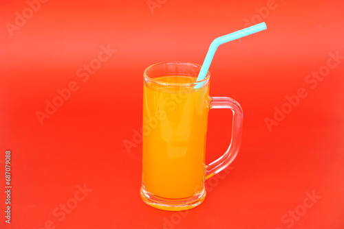 Glass mug of orange juice with drinking straw. Red  background. Concept, morning refreshing beverage. Sweet, testy and high vitamin C.         