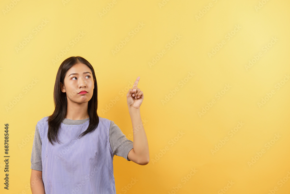 Young women points with finger up and doubtful face with empty space on isolated yellow background Young women points with finger up and doubtful face with empty space on isolated yellow background