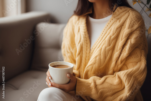 Woman wearing a warm pullover and holding a cup of coffee. Drink at morning. A girl in a cozy house drinks a hot drink.
