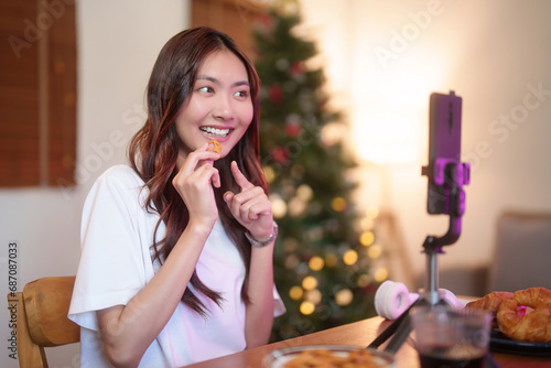 Young asian vj women use digital smartphone and recording video to speaking morning talks about news in live streaming on channel while eating snack and working with happiness at home studio photo