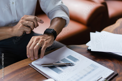 Hands of businessman checking time on smartwatch while working about financial document of business photo