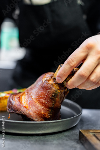 chef hand cooking Baked Pork knuckle with vegetables on plate in kitchen