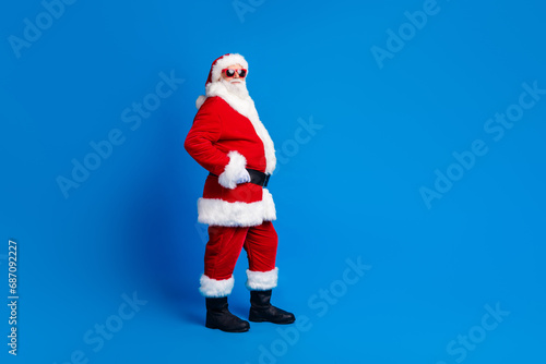 Full length photo of mature pensioner man touch belt shopping wear trendy santa claus costume coat isolated on blue color background © deagreez