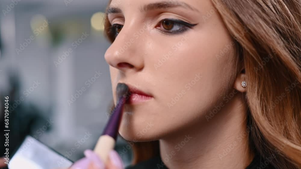 A makeup artist applies foundation to the model's lips with a special brush. Young woman in a beauty salon. A makeup artist applies foundation to the model's lips with a special brush. Young woman in a beauty salon.