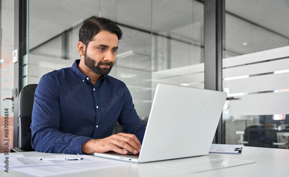 Busy professional Indian business man employee looking at laptop computer, businessman office worker or executive manager analyzing project strategy working online with ai software at work desk. Busy professional Indian business man employee looking at laptop computer, businessman office worker or executive manager analyzing project strategy working online with ai software at work desk.