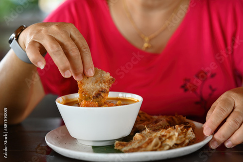 Close-up of woman s hand taking a food bite and eating chapati with Massaman curry