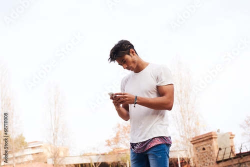 Standing man in  withe t-shirt texting a message using his mobile phone photo