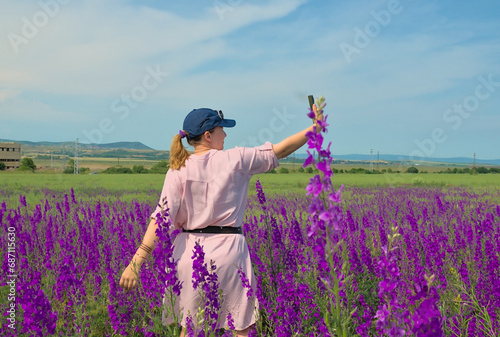 A girl in spring flowers in a field in nature poses for a blog. Purple field of Delphínium flowers