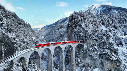 Fototapeta Naklejka Na Ścianę i Meble -  Snow falling and Train passing through famous mountain in Filisur, Switzerland. Train express in Swiss Alps snow winter scenery.