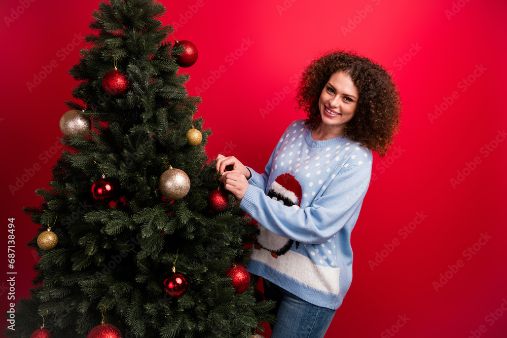 Photo of pretty cute girl dressed ugly christmas sweater hanging baubles decorating xmas tree isolated red color background Photo of pretty cute girl dressed ugly christmas sweater hanging baubles decorating xmas tree isolated red color background