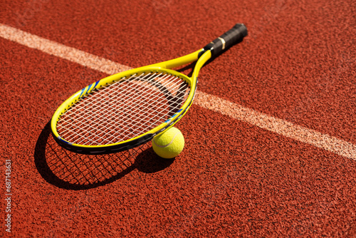 Racket with a tennis ball on a red clay court. © Angelov