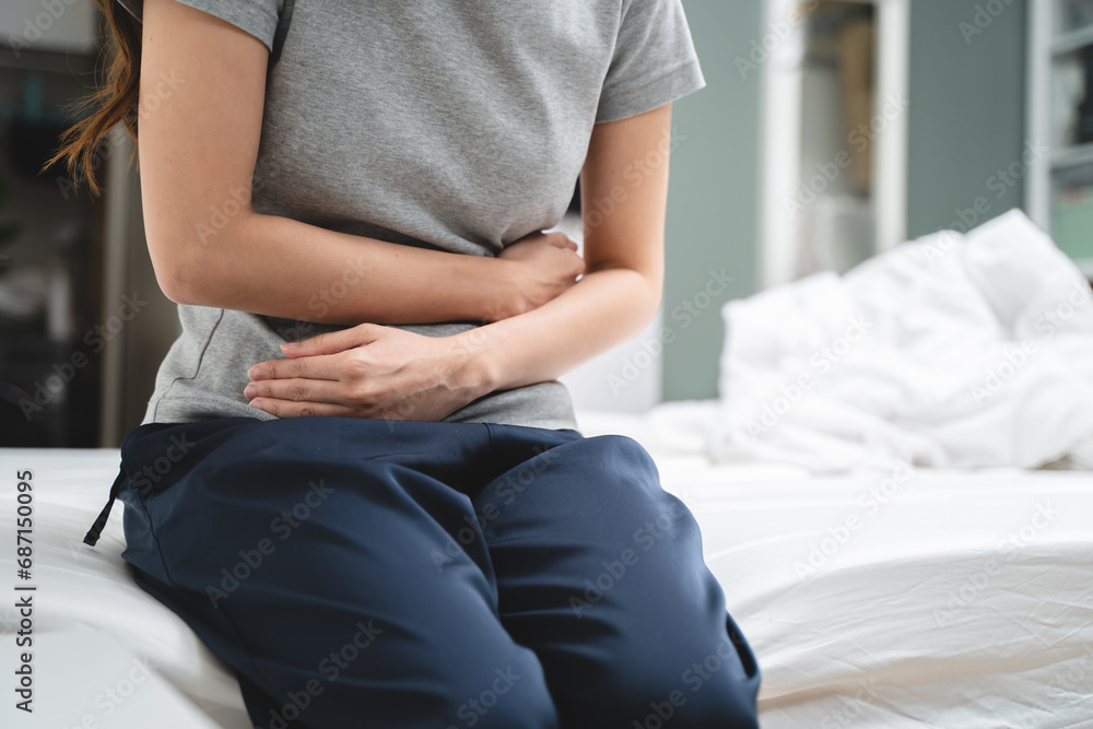 Menstruation symptom concept, Close-up woman touching her belly and feeling stomach pain from cycle period on the bed at home.