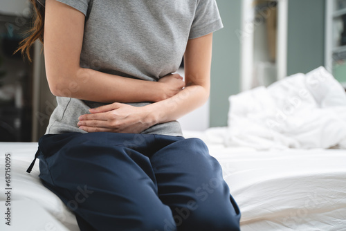 Menstruation symptom concept, Close-up woman touching her belly and feeling stomach pain from cycle period on the bed at home.