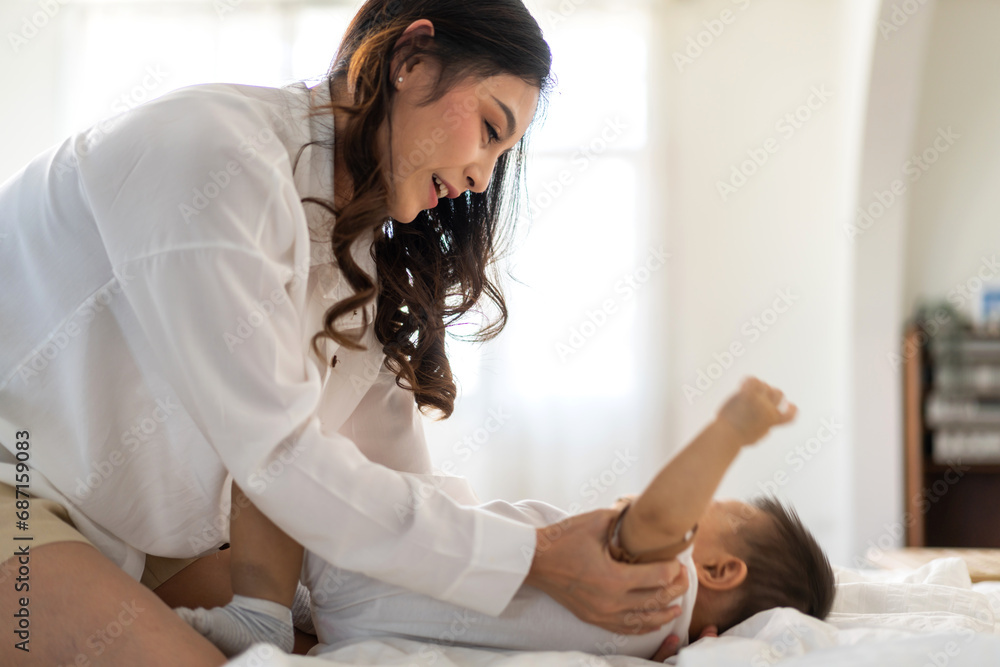 Obraz premium Portrait of enjoy happy love family asian mother playing with adorable little asian baby, newborn, infant.Mom touching care with cute son in a white bedroom.Love of family concept