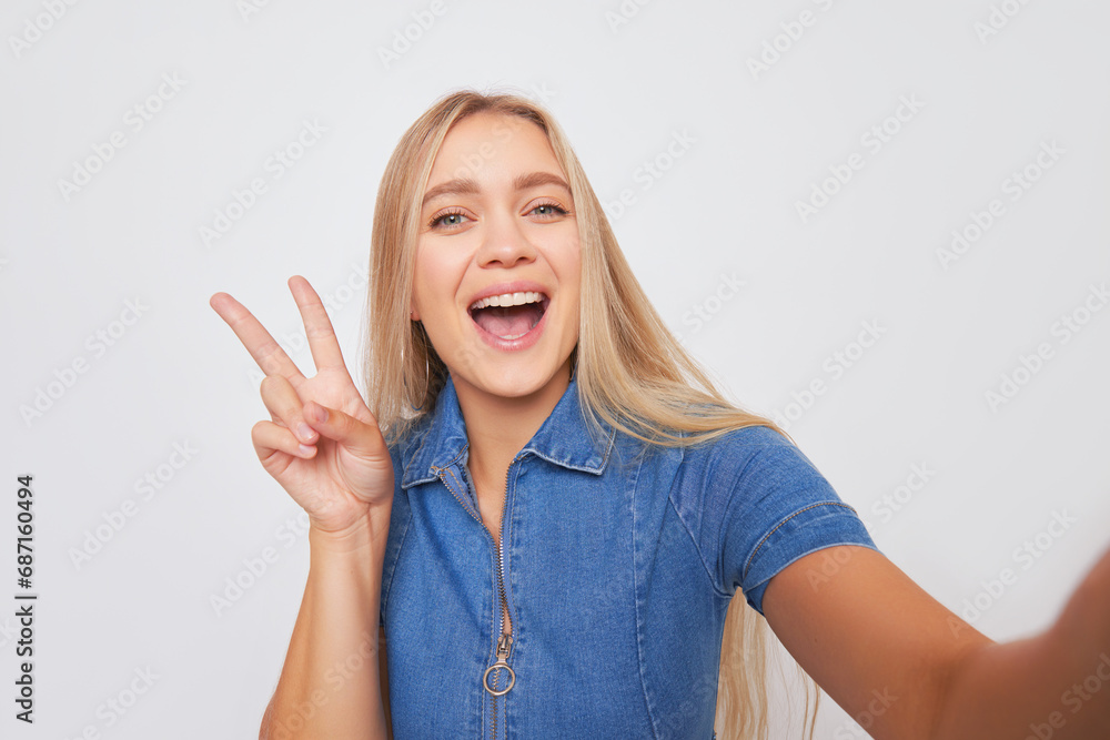 Selfie portrait fair-haired girl with long hair in denim blue shirt showing victory sign, good mood concept, copy space Selfie portrait fair-haired girl with long hair in denim blue shirt showing victory sign, good mood concept, copy space