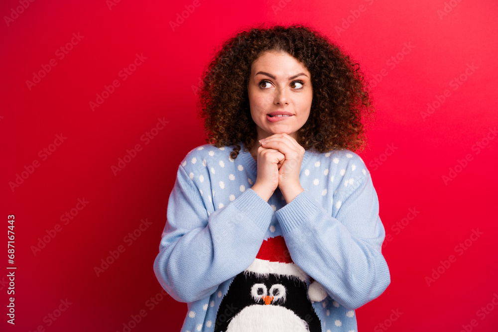 Photo of doubtful unsure girl dressed ugly christmas sweater hands chin biting lip looking empty space isolated red color background