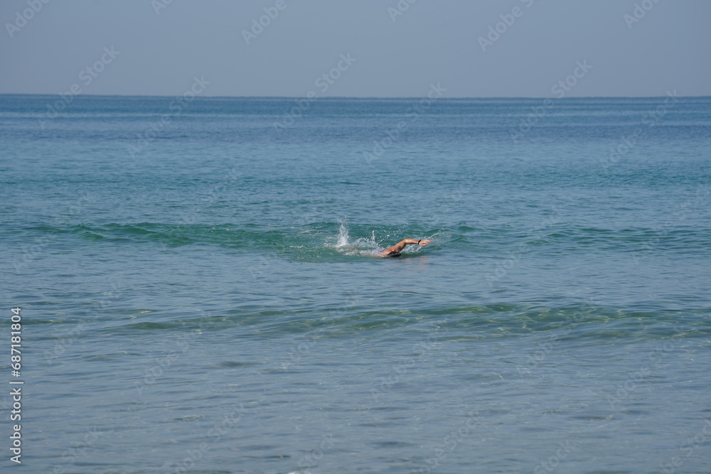 Young strong athletic man swimming in the sea under the sunshine. Sport' vacation healthy lifestyle. Mediterranean Sea in winter