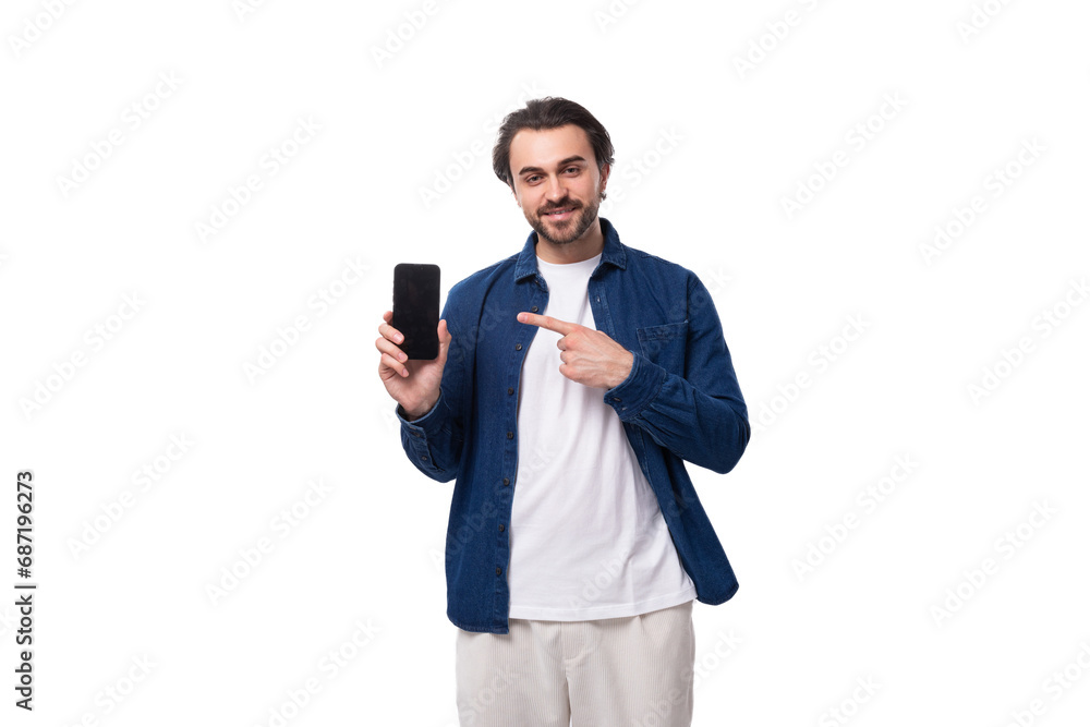 a young handsome brutal brunette guy in a denim shirt shows the screen of a mobile phone. e-business advertising concept a young handsome brutal brunette guy in a denim shirt shows the screen of a mobile phone. e-business advertising concept