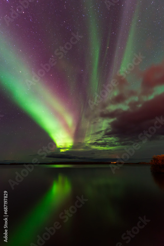Fototapeta Naklejka Na Ścianę i Meble -  Captured on the tranquil shores of Pinehouse Lake, Canada, this mesmerizing scene unfolds as the Northern Lights dance gracefully across the night sky.  