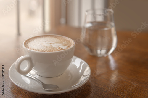 A cup of coffee and a glass of water stands on a wooden table