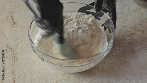 Mixing flour and eggs to obtain shortbread. A chef mixes flour with egg yolks in a glass bowl with a silicone spatula. Dynamic shooting