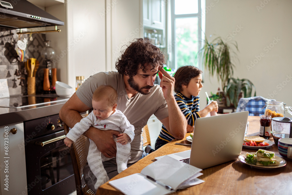 Busy father with baby working from home on laptop Busy father with baby working from home on laptop