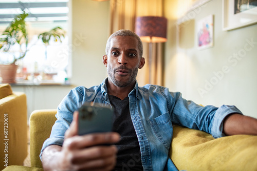 Man sitting on couch looking surprised at phone photo