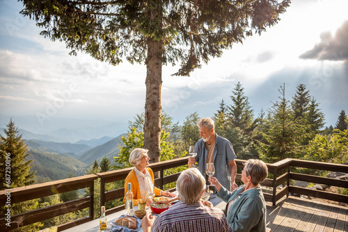 Group of seniors enjoying dinner with wine on mountain cabin deck photo