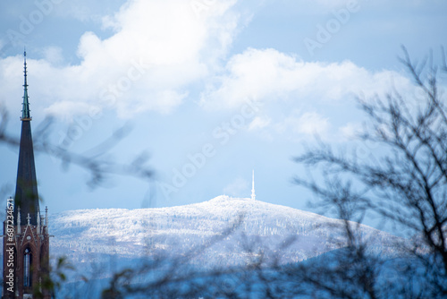 winter, church tower in the foreground, in the background on a snow-covered mountain the tower and the forest
