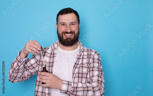 Bearded man with skincare, cosmetics and dermatology against a blue studio background. Male person, model and guy with oil, beauty and liquid for face, grooming and routine for smooth skin. Beard oil.