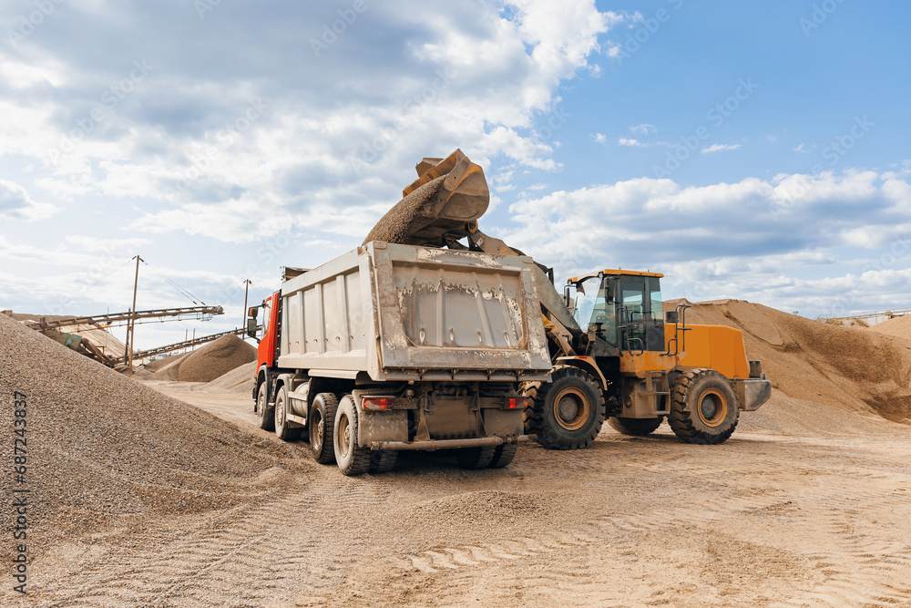 Obraz premium Yellow Excavator loading sand to industrial truck on industry quarry. Construction site open pit mine concept