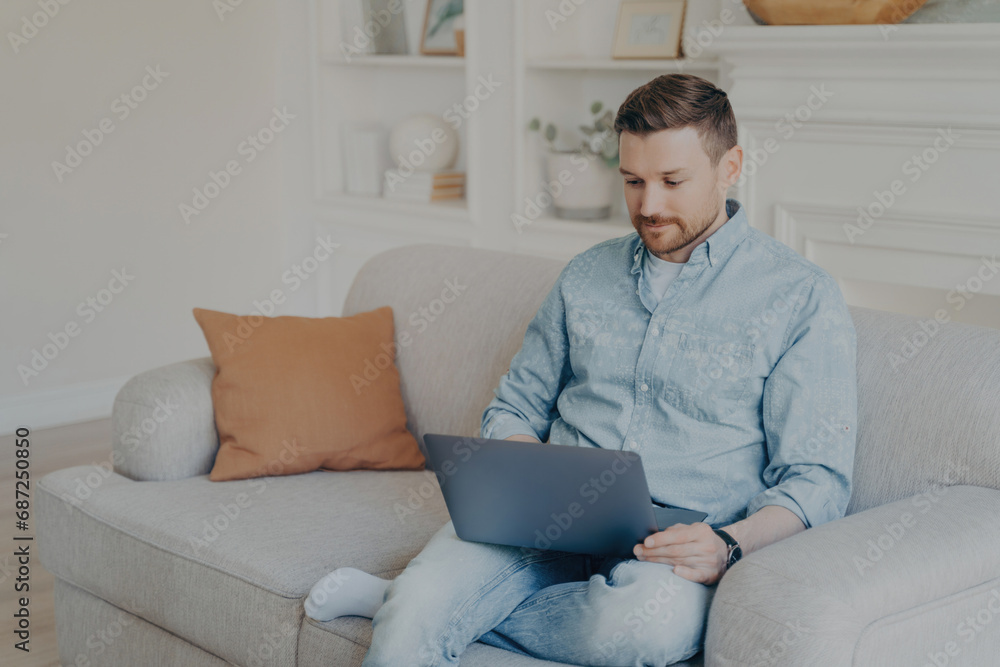 Man in casual wear focused on his laptop, comfortably working from home on a cozy couch Man in casual wear focused on his laptop, comfortably working from home on a cozy couch