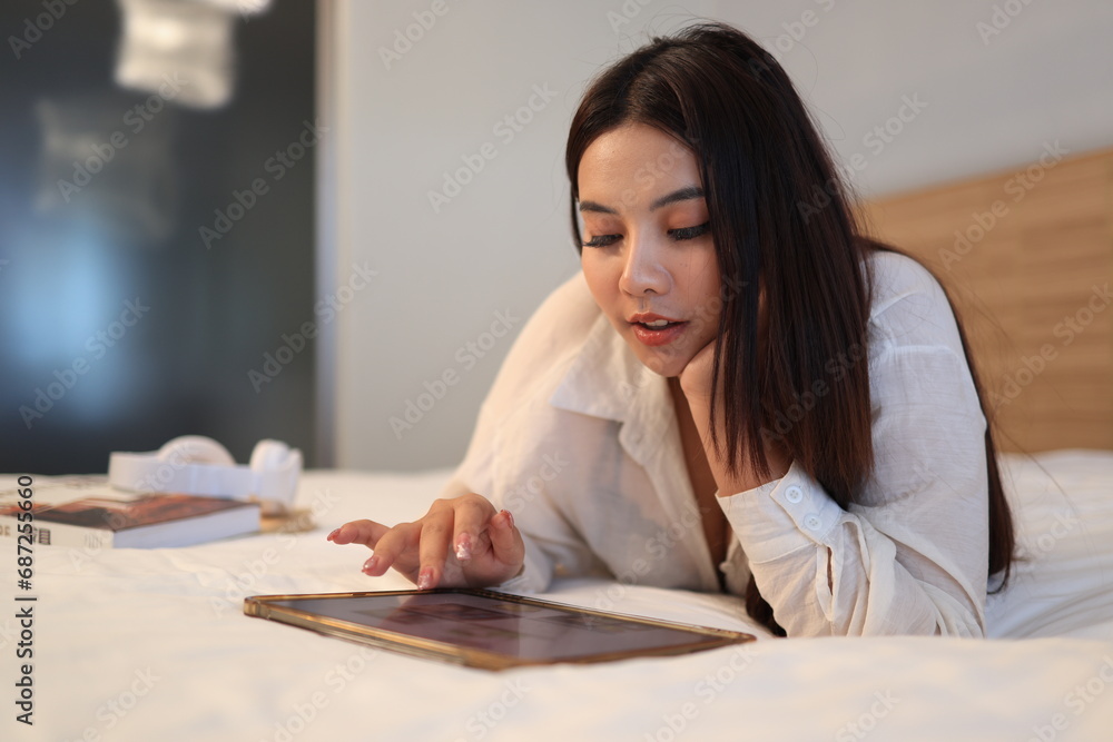 Asian beautiful woman playing tablet on the bed at bedroom, addicted to social media Asian beautiful woman playing tablet on the bed at bedroom, addicted to social media