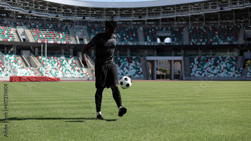 African American man playing football on the stadium field. A man runs with a soccer ball across the field.