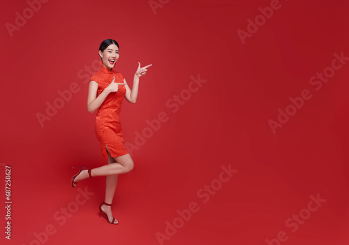 Happy Chinese new year. Asian woman wearing traditional cheongsam qipao dress and hands pointing finger isolated on red copy space background.