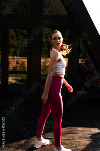 Vertical portrait of pretty female workout before fitness training session at country house building exterior. Healthy young woman warming up outdoors on summer morning. Concept of wellness  fitness