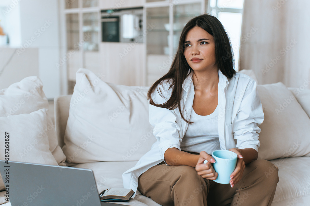 bored brunette is sitting at home on the couch with a laptop and diary. She is tired of working at home during pandemic wants to communicate with people. frustrated young woman suffering loneliness bored brunette is sitting at home on the couch with a laptop and diary. She is tired of working at home during pandemic wants to communicate with people. frustrated young woman suffering loneliness